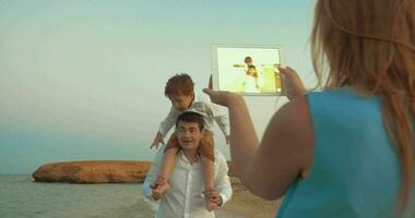 Mother with pad shooting father and son on beach video