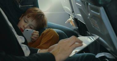 garçon en utilisant intelligent téléphone et père avec tablette dans avion video