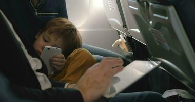 Child with cell and and man using pad in plane video