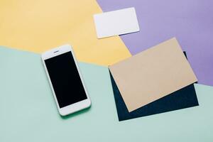 Creative flat lay style workspace desk with smartphone and blank envelope and name card on modern colorful background photo