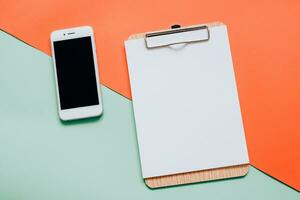 Creative flat lay of smartphone and blank clipboard on minimal color background photo