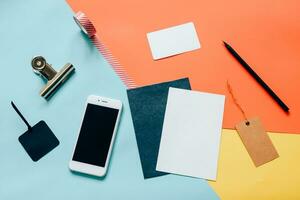 Creative flat lay style workspace desk with smartphone, blank envelope, tag and masking tape on modern colorful background photo