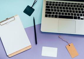 Top view flat lay style of worksapce desk with laptop, blank clipboard and tag on minimal color background photo