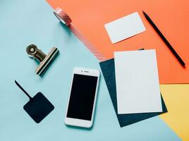 Creative flat lay style workspace desk with smartphone, blank envelope, tag and masking tape on modern colorful background photo