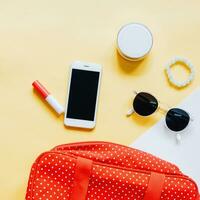 Flat lay of red polka dot woman bag open out with cosmetics, accessories and smartphone on colorful background photo