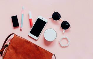 Flat lay of brown leather woman bag open out with cosmetics, accessories and smartphone on pink background with copy space photo