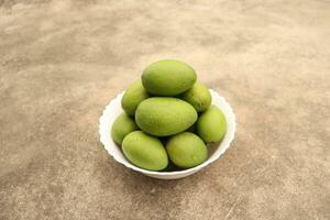 Raw green mango on white bowl photo