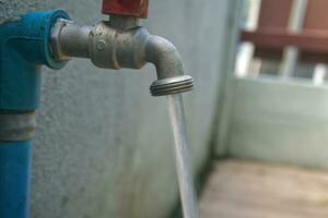 metal grifo con azul tubo giro en dejar el agua desagüe lejos difuminar antecedentes No gente. concepto para ambiente y escasez agua en mundo para agua día con copyspace foto