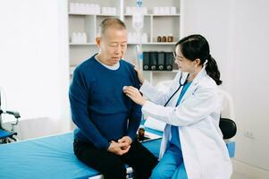 Asian doctor in white suit take notes while discussing and Asian elderly, man patient who lying on bed with receiving saline solution in hospital photo