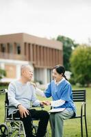 Elderly asian senior man on wheelchair with Asian careful caregiver and encourage patient, walking in garden. with care from a caregiver and senior health insurance. photo