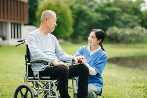 Elderly asian senior man on wheelchair with Asian careful caregiver. Nursing home hospital garden concept. photo