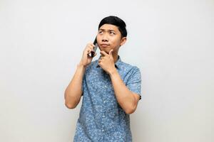 asiático hombre azul camisa utilizando móvil teléfono y pensando para decidir alguna cosa aislado foto