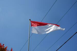 el rojo y blanco indonesio bandera es volador en contra un antecedentes de azul cielo y cables foto