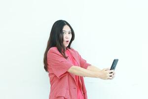 portrait of beautiful asian woman wearing red outfit holding mobile phone with surprised expression photo