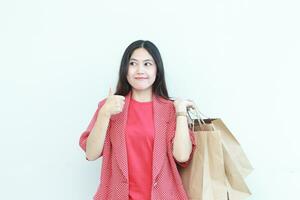 portrait of beautiful asian woman wearing red outfit gesturing carrying lots of shopping bags with happy expression photo