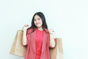 retrato de hermosa asiático mujer vistiendo rojo atuendo gesticulando que lleva un montón de compras pantalones con contento expresión foto