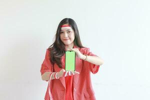 portrait of beautiful asian woman wearing red outfit celebrating Indonesia independence day holding mobile phone and smiling photo