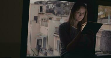 Woman using tablet PC sitting on windowsill video