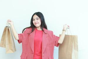 portrait of beautiful asian woman wearing red outfit gesturing carrying lots of shopping bags with happy expression photo