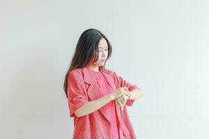 portrait of beautiful asian woman wearing red outfit gesturing looking at clock and smiling photo