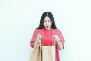 portrait of beautiful asian woman wearing red outfit with surprised gesture looking at contents of shopping bag photo