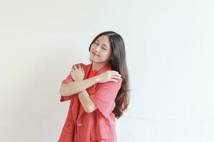 portrait of beautiful asian woman wearing red outfit hugging herself while smiling photo