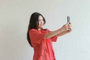 portrait of beautiful asian woman wearing red outfit looking at mobile phone with happy expression photo