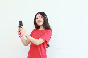 retrato de hermosa asiático mujer vistiendo rojo atuendo celebrando Indonesia independencia día participación móvil teléfono y sonriente foto