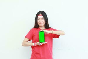 portrait of beautiful asian woman wearing red outfit celebrating Indonesia independence day by gesturing holding mobile phone photo