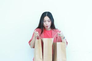 portrait of beautiful asian woman wearing red outfit with surprised gesture looking at contents of shopping bag photo