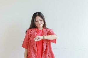 portrait of beautiful asian woman wearing red outfit gesturing looking at clock and smiling photo