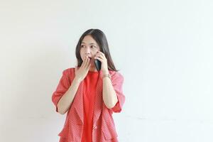 portrait of beautiful asian woman wearing red outfit while calling with surprised expression photo