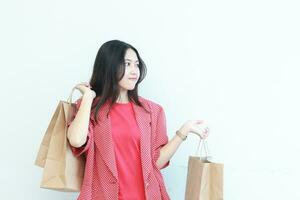 portrait of beautiful asian woman wearing red outfit gesturing carrying lots of shopping bags with happy expression photo
