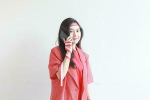 portrait of beautiful asian woman wearing red outfit celebrating Indonesia independence day while calling with smiling expression photo
