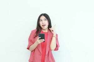 portrait of beautiful asian woman wearing red outfit while holding mobile phone with happy expression photo