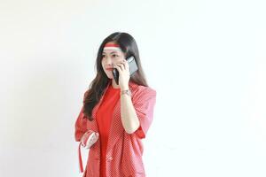 portrait of beautiful asian woman wearing red outfit celebrating Indonesia independence day while calling with smiling expression photo