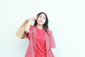 portrait of beautiful asian woman wearing red outfit gesturing carrying lots of shopping bags with thinking expression photo