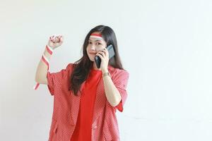 portrait of beautiful asian woman wearing red outfit celebrating Indonesia independence day while calling with smiling expression photo