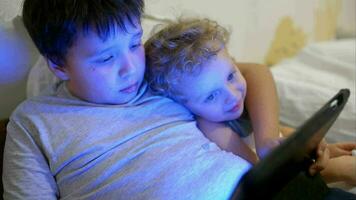 Two boys in bed with touch pad One playing game, another watching video