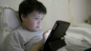 adolescente chico utilizando tableta computadora acostado en cama video