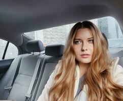 Young woman with long hair, wavy hairstyle in the car or taxi cab as passenger, exploring the city, transport and travel photo