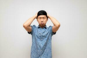 asiático hombre azul camisa participación cabeza siente duda y mareado con trabajando aislado foto