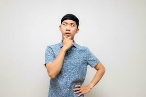 joven asiático hombre azul camisa posando pensando y siente vacilar aislado foto