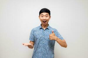 Positive asian man blue shirt amazed show thumb up with empty hand up isolated photo