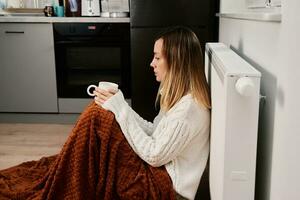 preocupado mujer sentar cerca calefacción radiador debajo cobija con taza de té foto