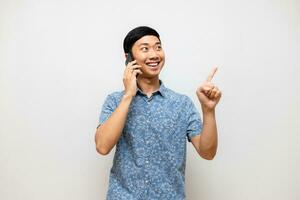 Positive asian man blue shirt holding mobile phone smile and gesture point finger isolated photo