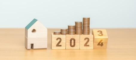 2023 flipping to 2024 year block with house model and Coins stack. real estate, Home loan, tax, investment, mortgage, financial, savings and New Year Resolution concepts photo