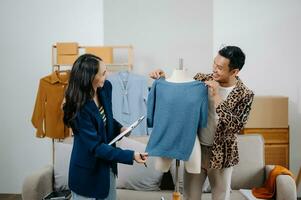 Couple of fashion designers working with fabric and clothing sketches at the studio full of tailoring tools and holds tablet and laptop. photo