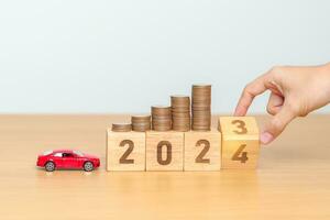 2023 flipping to 2024 year block with car model and Coins Money stack for deposit and Automobile Tax. Money Saving, Car Insurance, Financial, vehicle Repair and Maintenance and New Year concept photo
