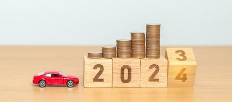 2023 flipping to 2024 year block with car model and Coins Money stack for deposit and Automobile Tax. Money Saving, Car Insurance, Financial, vehicle Repair and Maintenance and New Year concept photo